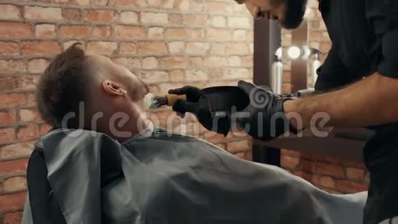 理发师将泡沫涂在男性脸上用于男性沙龙的湿胡须剃须为客户准备湿剃须膏视频的预览图