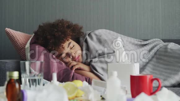 生病的非裔美国女孩正躺在温暖的格子布下的公寓里躺在沙发上休息视频的预览图