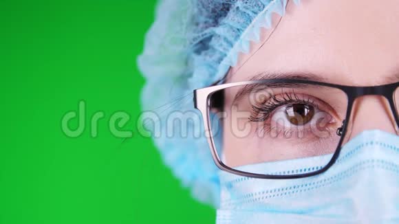 绿色背景特写镜头眼睛部分女医生脸戴眼镜戴蓝色医用面罩和医用帽视频的预览图