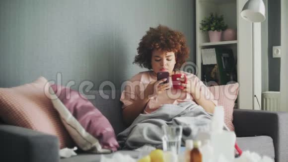 生病的非洲裔美国年轻女孩在家里打电话喝热茶视频的预览图