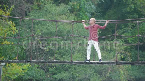 迷人的金发帅哥站在美丽的画报之处的河悬桥上视频的预览图