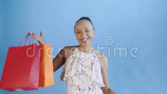 非洲裔美国妇女的肖像正在工作室的蓝色背景上用购物袋跳舞幸福的女人视频的预览图