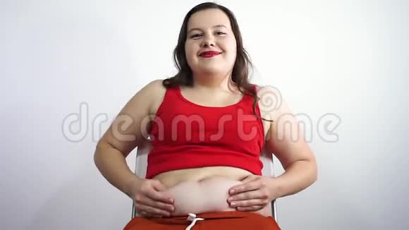 胖姑娘坐在椅子上摸着肚子上的脂肪微笑视频的预览图