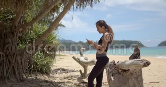 在海滩上锻炼时使用智能手机的性格开朗的女运动员视频的预览图