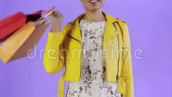 美国黑人妇女在工作室的紫色背景上带购物袋的肖像幸福的女人手里拿着视频的预览图