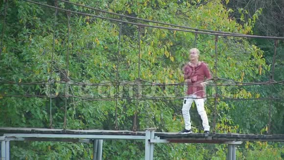 在美丽的画报中迷人的金发女郎站在河上的吊桥上跳舞唱歌视频的预览图