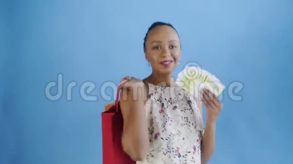 一个非洲裔美国妇女带着钱卡和购物袋蓝色背景带花的白色连衣裙视频的预览图