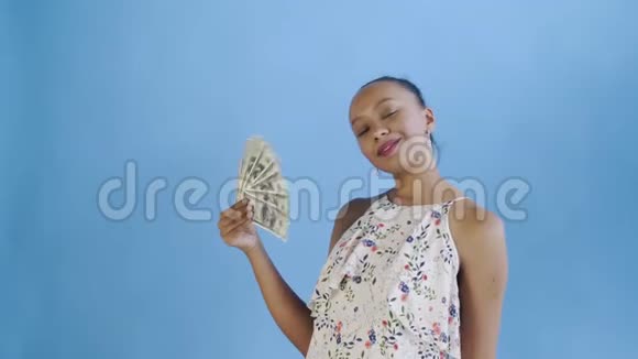 一位非洲裔美国妇女在录音室里用蓝色背景的钱扇子带花的白色连衣裙视频的预览图