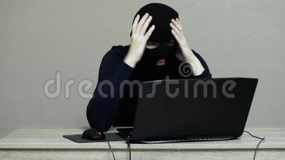 穿着黑色面具的搞笑男黑客巴拉克拉娃对笔记本电脑进行黑客攻击看着摄像头视频的预览图