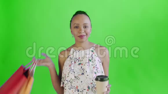 一位非洲裔美国妇女拿着购物袋在工作室里喝着绿色背景的咖啡JWhite连衣裙视频的预览图