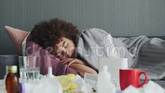 生病的非裔美国女孩正躺在温暖的格子布下的公寓里躺在沙发上休息视频的预览图