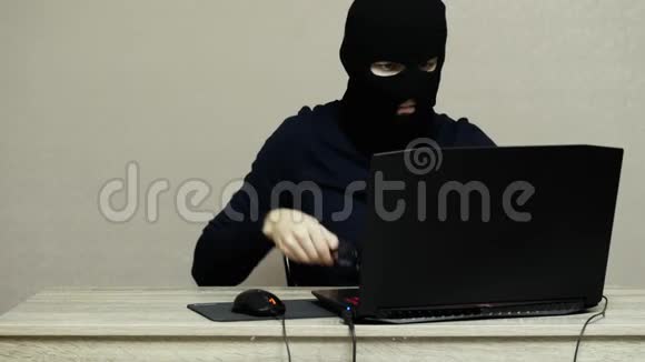 戴黑色面具的男性黑客巴拉克拉瓦戴上眼镜对笔记本电脑进行黑客攻击视频的预览图