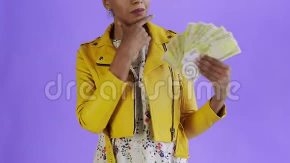 体贴成功的非裔美国妇女与金钱爱好者紫色背景工作室黄色夹克视频的预览图
