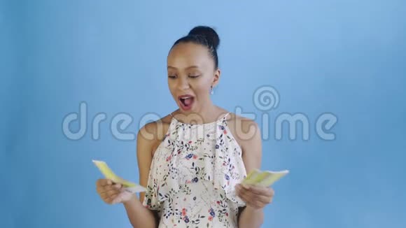 漂亮的非裔美国妇女正以蓝色为背景数钱带花的白色裙子视频的预览图