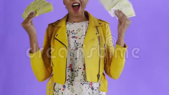 满意的兴奋的兴奋的非裔美国女人在紫色背景的黄色夹克上展示金钱说上帝啊视频的预览图