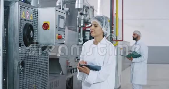 有魅力的成熟女工程师分析了制造业中的工业机器她记下了她的笔记视频的预览图