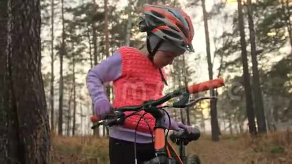 孩子戴头盔一个高加索儿童在秋季公园骑自行车在森林里骑着黑色橙色自行车的小女孩视频的预览图