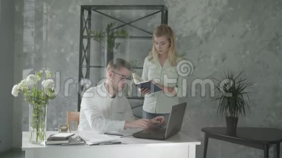 实习一个年轻的商务女性手里拿着一本书教一个坐在笔记本电脑上的实习生员工关系视频的预览图