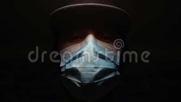 黑色背景下戴医用外科流感面罩的患病青年的深色肖像视频的预览图