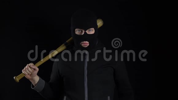 一个戴着巴拉克拉瓦面具的人正拿着棒球棒站着一个强盗拿着棒球棒站在黑色的背景上视频的预览图