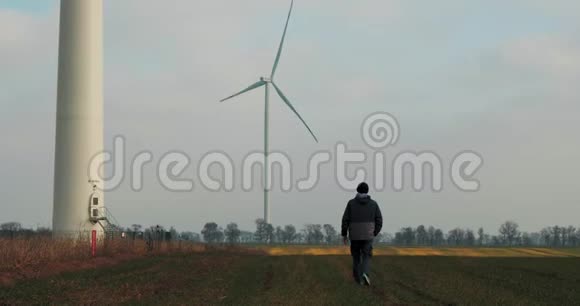 一个男人在后台旋转风车的田野里行走风的力量清洁和可再生能源解决方案风力涡轮机视频的预览图