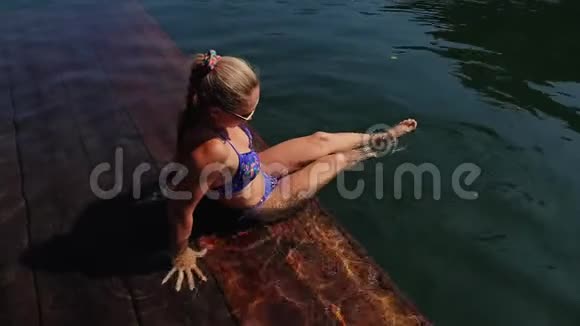 女人戴着太阳镜和泳衣坐在日光浴床上女孩在洪水木水下码头休息路面是视频的预览图