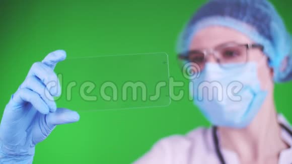 绿色背景特写镜头医生戴着医疗帽口罩蓝色医疗手套拿着玻璃卡点击视频的预览图