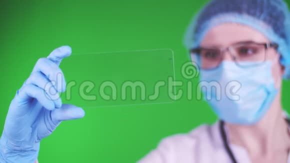 绿色背景特写镜头医生戴着医疗帽口罩蓝色医疗手套手里拿着一张玻璃卡片视频的预览图
