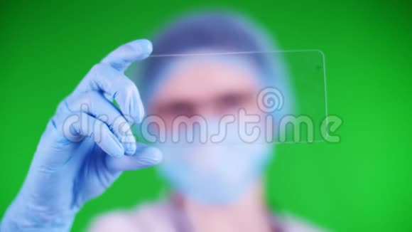 绿色背景特写镜头医生戴着医疗帽口罩蓝色医疗手套手里拿着一张玻璃卡片视频的预览图