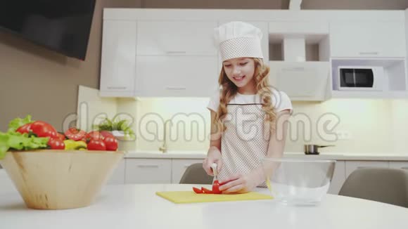 穿着厨房围裙和帽子的可爱女孩切番茄做沙拉视频的预览图