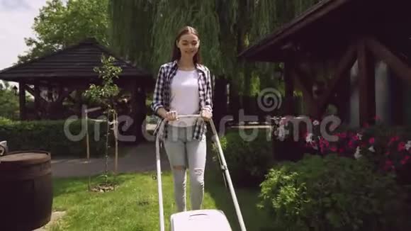 快乐的黑发女孩推草割草机靠近木制露台视频的预览图