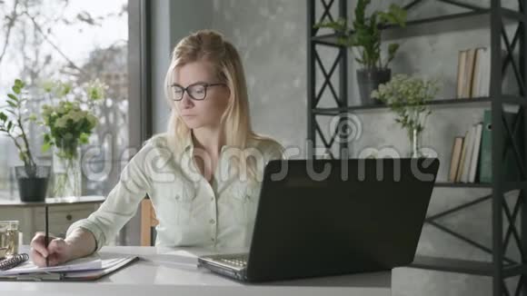 在笔记本电脑上工作的漂亮金发女商人使用应用程序在线银行在电脑上远程工作的年轻女性视频的预览图