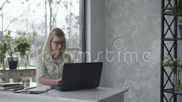 快乐的女企业家戴着眼镜带着笔记本电脑坐在桌边享受商业成功快乐视频的预览图