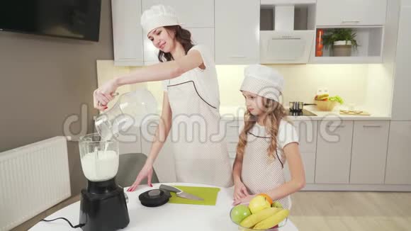 快乐的母亲和漂亮的女儿在搅拌机里做奶昔视频的预览图