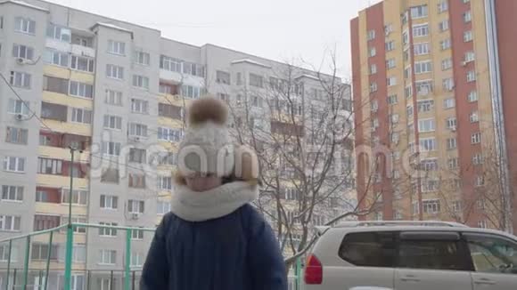 穿着白色帽子围巾和外套的悲伤少年女孩在冬天的街道上看着什么走路的女孩在看视频的预览图