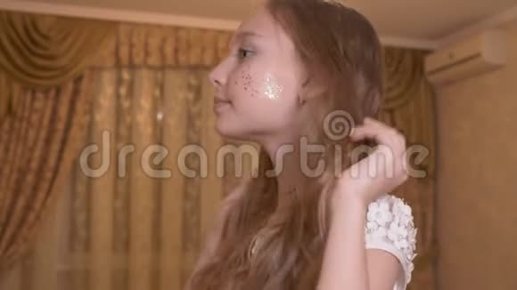 肖像年轻女孩与闪亮的化妆脸触摸卷发在卧室的窗户背景美丽少女少年视频的预览图