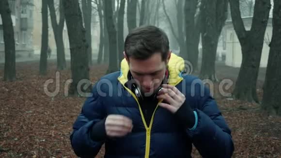 男运动员在城市公园里戴上无线耳机寒冷的雾天早晨视频的预览图