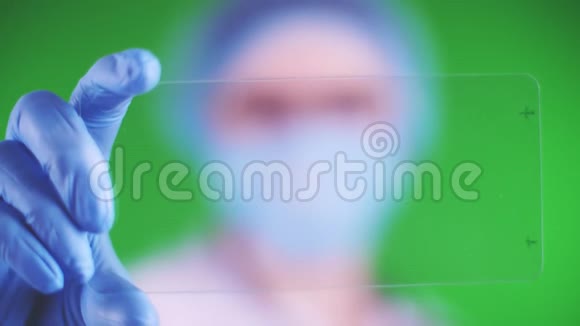 绿色背景特写镜头医生戴着医疗帽口罩蓝色医疗手套拿着玻璃卡点击视频的预览图