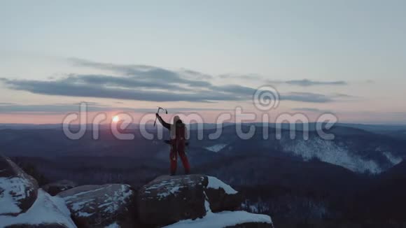 一个孤独的雄性登山者站在山顶上得意洋洋地举起手来欣赏日落视频的预览图