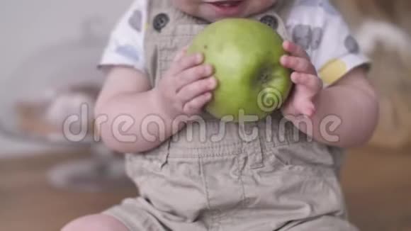可爱的蹒跚学步的小男孩拿着大绿苹果有趣地试图吃视频的预览图