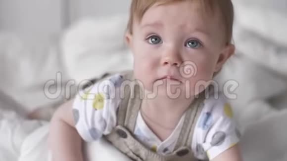 可爱的小男孩蹒跚学步好奇地爬行在家里的白色床上享受乐趣视频的预览图