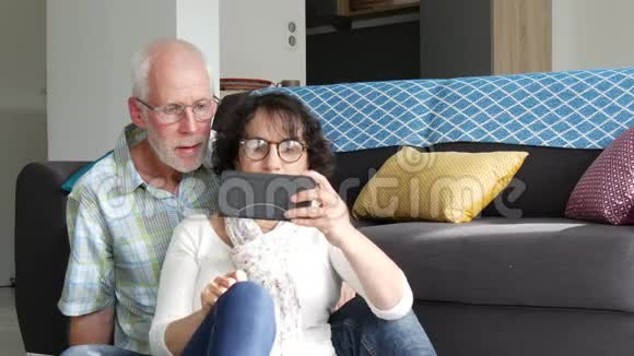 成熟有魅力的情侣坐在沙发上使用智能手机视频的预览图