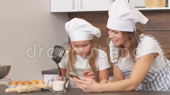 可爱的女儿手里拿着锅铲看着手机寻找蛋糕的配方视频的预览图