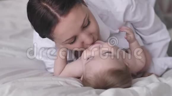 快乐的妈妈吻着她的小男孩笑了一起躺在床上幸福的家庭母亲视频的预览图