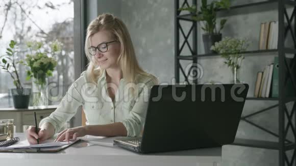 快乐的微笑着的女人在电脑前工作带着鲜花来到办公室为成功而高兴视频的预览图
