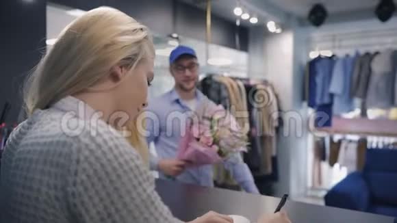 在快递服务中工作的男性会给顾客带来漂亮的花束和支票订单年轻女性视频的预览图