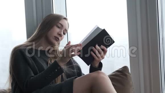 年轻漂亮的女孩在窗边看书视频的预览图