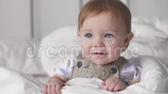 可爱的小白种人男孩微笑肖像婴儿在家里的床上笑视频的预览图