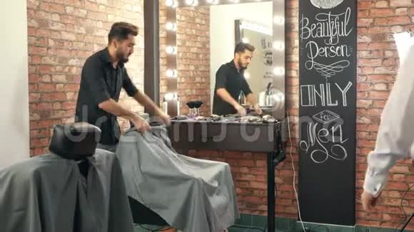 理发师邀请男性客户坐在理发店的椅子上视频的预览图