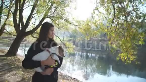 女孩带着狗走路指着湖和五颜六色的公园视频的预览图